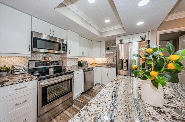 kitchen featuring white cabinets, a raised ceiling, crown molding, light hardwood / wood-style flooring, and stainless steel appliances