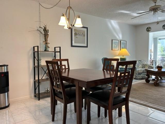 dining space with a textured ceiling, light colored carpet, and ceiling fan with notable chandelier