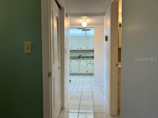 hallway with light tile patterned flooring, sink, and a textured ceiling