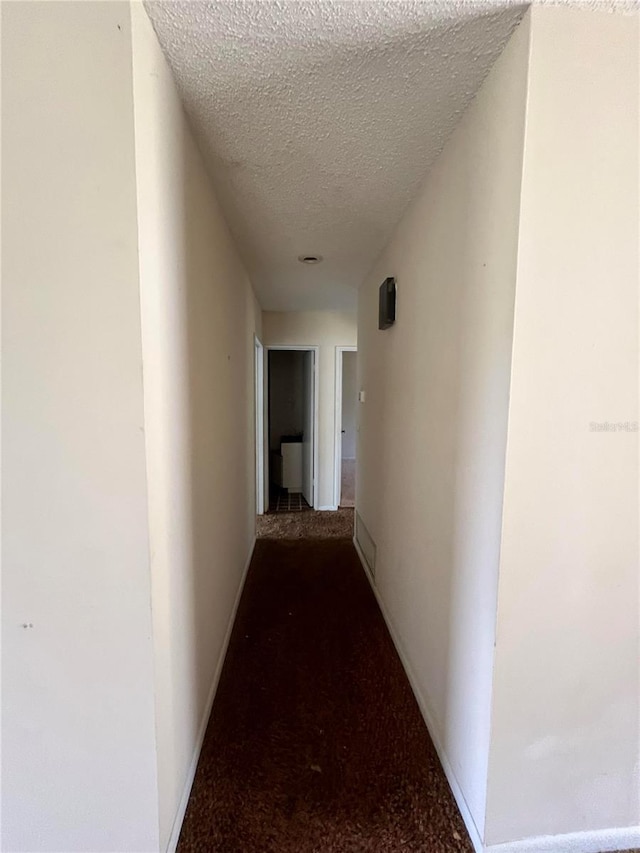 hallway with carpet flooring and a textured ceiling