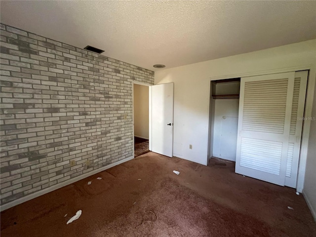 unfurnished bedroom with dark colored carpet, a textured ceiling, brick wall, and a closet