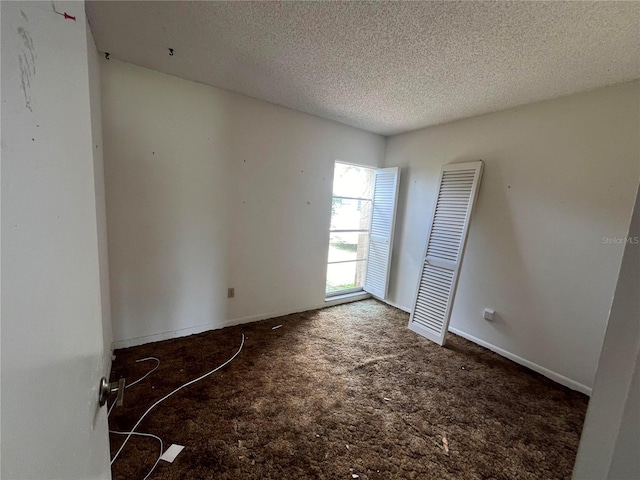 unfurnished room with dark carpet and a textured ceiling