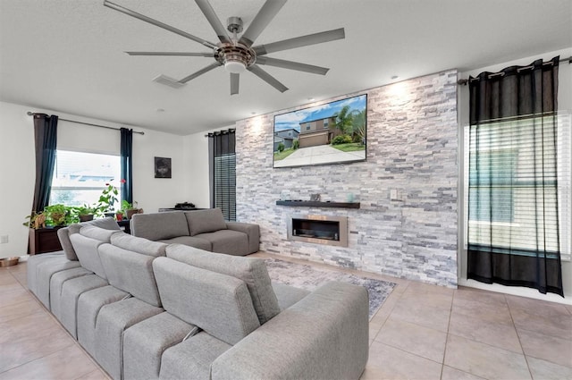 living room with a stone fireplace, ceiling fan, light tile patterned flooring, and a textured ceiling