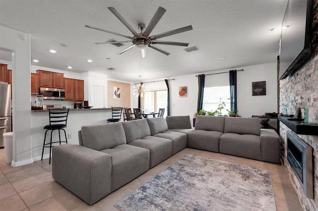 living room with a textured ceiling, a fireplace, light tile patterned floors, and ceiling fan with notable chandelier