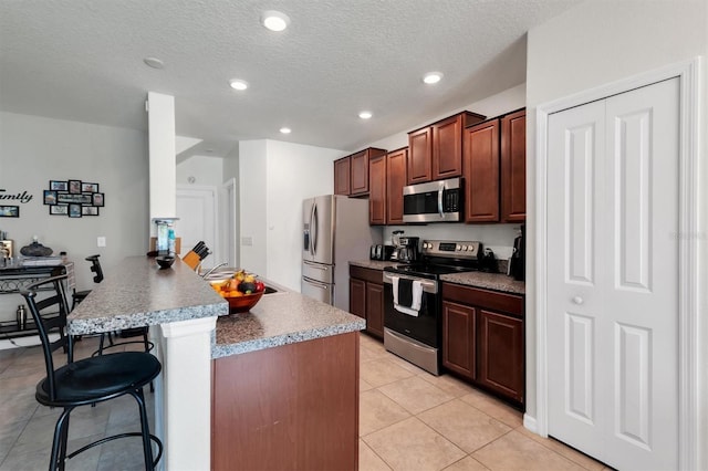 kitchen featuring a breakfast bar area, light tile patterned floors, a textured ceiling, and appliances with stainless steel finishes