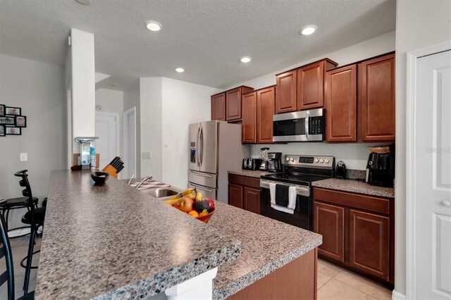 kitchen featuring appliances with stainless steel finishes, a textured ceiling, sink, light tile patterned floors, and a breakfast bar area