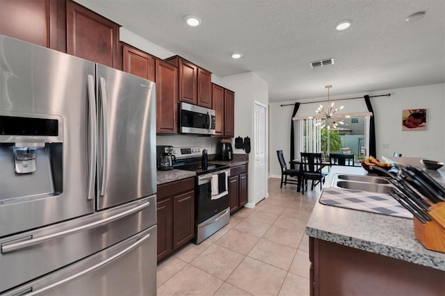 kitchen with appliances with stainless steel finishes, sink, light tile patterned floors, decorative light fixtures, and a chandelier