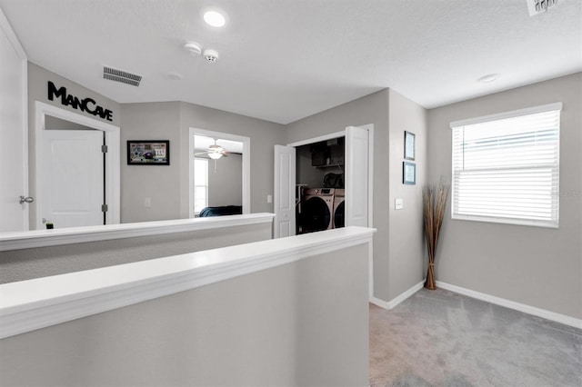 corridor with light colored carpet, a textured ceiling, and washing machine and clothes dryer