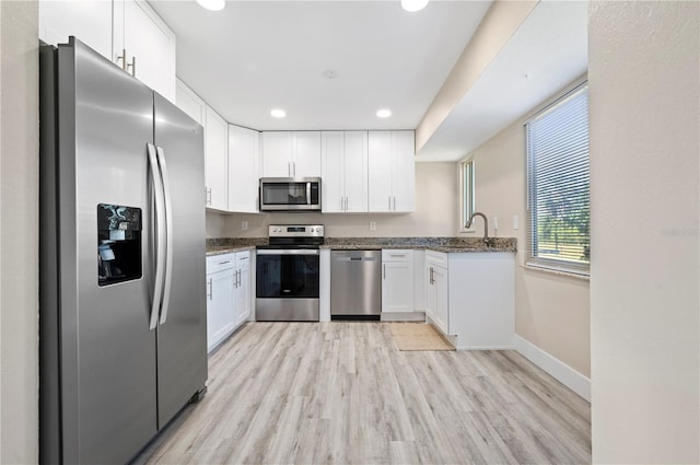 kitchen featuring stainless steel appliances, white cabinetry, light hardwood / wood-style floors, and dark stone counters