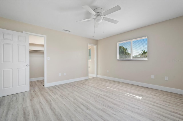 unfurnished bedroom with a walk in closet, light wood-type flooring, ceiling fan, and a closet