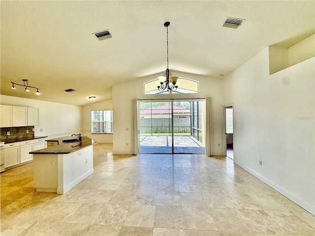 kitchen with a kitchen island with sink, pendant lighting, an inviting chandelier, sink, and vaulted ceiling