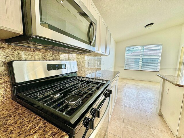 kitchen featuring vaulted ceiling, appliances with stainless steel finishes, white cabinetry, decorative backsplash, and a textured ceiling