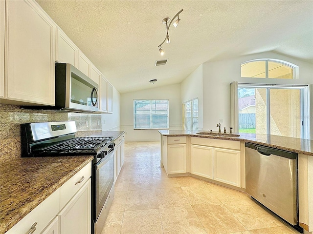 kitchen featuring stone countertops, a textured ceiling, sink, appliances with stainless steel finishes, and lofted ceiling