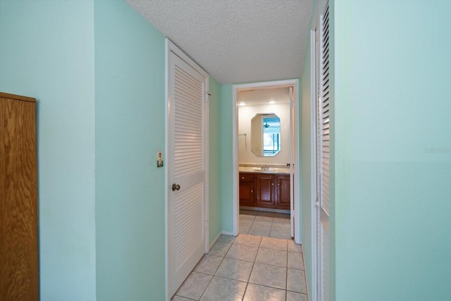 corridor with sink, light tile patterned floors, and a textured ceiling