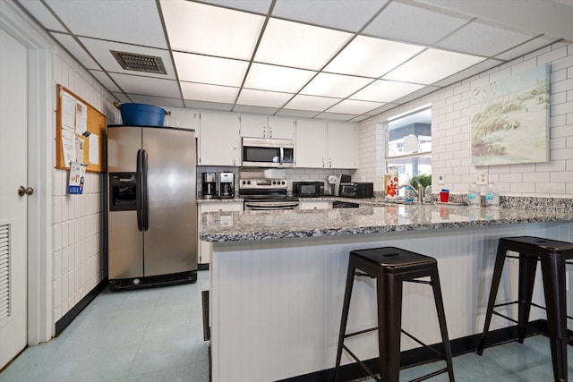 kitchen featuring appliances with stainless steel finishes, a paneled ceiling, white cabinetry, and light stone counters