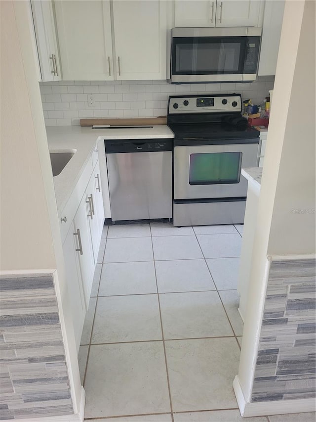 kitchen with tasteful backsplash, white cabinets, sink, light tile floors, and appliances with stainless steel finishes