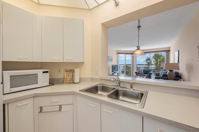 kitchen with hanging light fixtures, white cabinetry, sink, and a textured ceiling