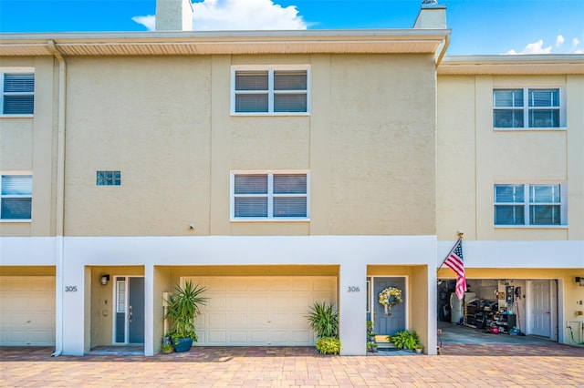 townhome / multi-family property with driveway, a chimney, an attached garage, and stucco siding