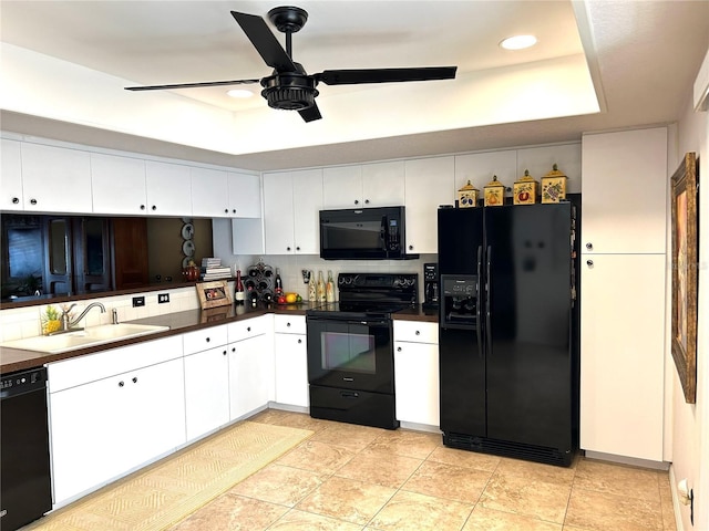 kitchen featuring a tray ceiling, backsplash, white cabinetry, a sink, and black appliances