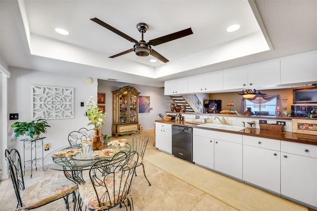 kitchen with a sink, white cabinetry, black dishwasher, dark countertops, and a raised ceiling