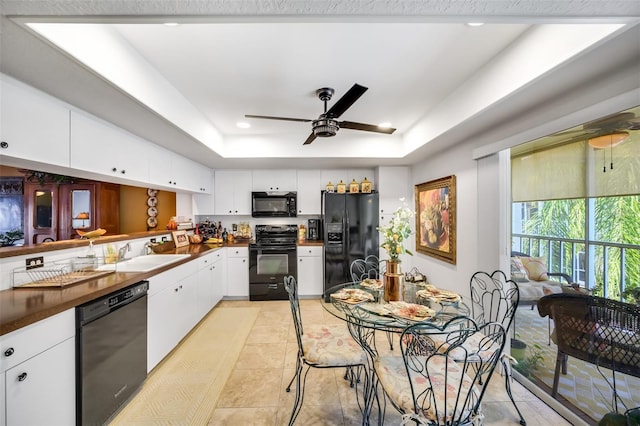 kitchen with a sink, white cabinetry, black appliances, a tray ceiling, and dark countertops