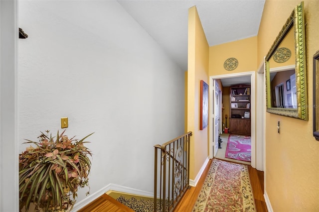 corridor featuring an upstairs landing, baseboards, and wood finished floors