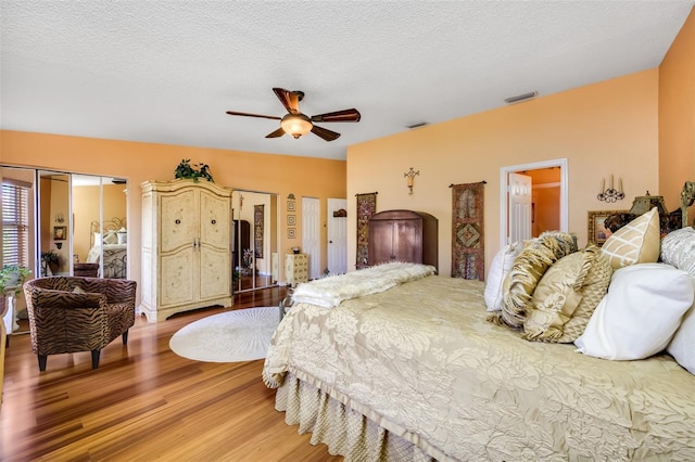 bedroom with a ceiling fan, visible vents, a textured ceiling, and wood finished floors