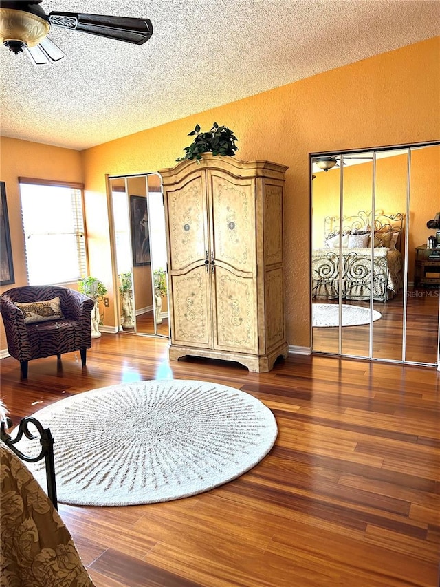 interior space with a ceiling fan, a textured wall, a textured ceiling, and wood finished floors