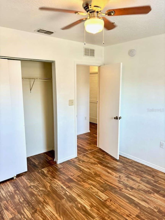 unfurnished bedroom with ceiling fan, a closet, dark wood-type flooring, and a textured ceiling