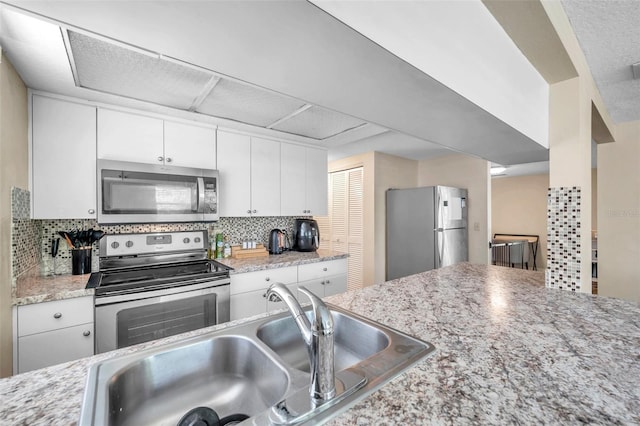 kitchen with backsplash, white cabinets, sink, light stone countertops, and stainless steel appliances