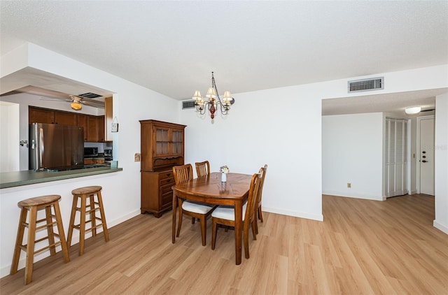 dining room with light hardwood / wood-style floors, a textured ceiling, and ceiling fan with notable chandelier