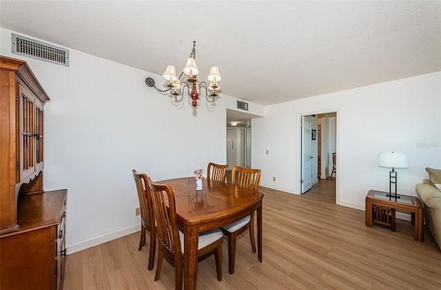 dining space with a textured ceiling, a chandelier, and light hardwood / wood-style flooring