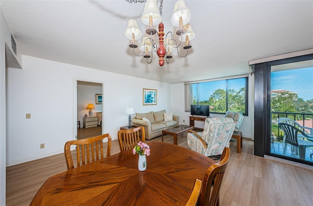 dining area with a wall of windows, a textured ceiling, a chandelier, and light hardwood / wood-style floors