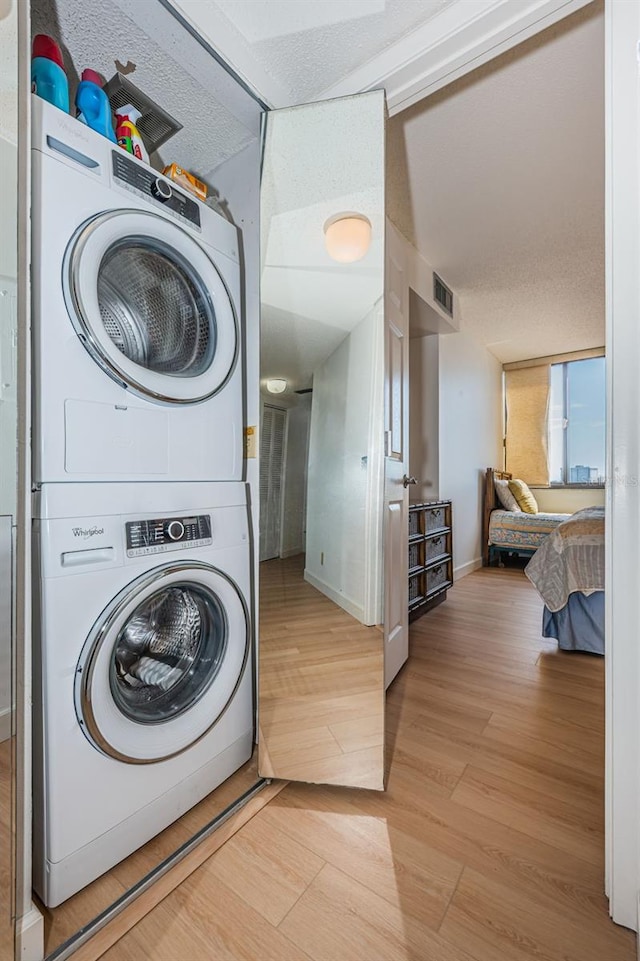 clothes washing area featuring light hardwood / wood-style floors and stacked washer / dryer