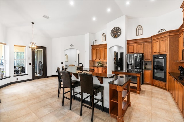 kitchen featuring tasteful backsplash, stainless steel fridge with ice dispenser, double oven, pendant lighting, and a center island with sink