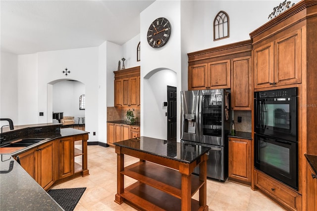 kitchen with sink, stainless steel refrigerator with ice dispenser, backsplash, black double oven, and dark stone counters