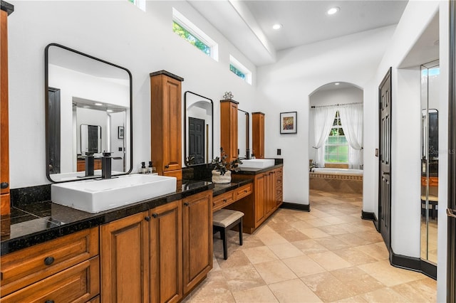 bathroom with tile patterned floors, tiled tub, vanity, and a high ceiling