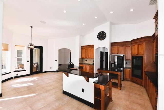 kitchen featuring a breakfast bar, an island with sink, stainless steel fridge, hanging light fixtures, and black double oven