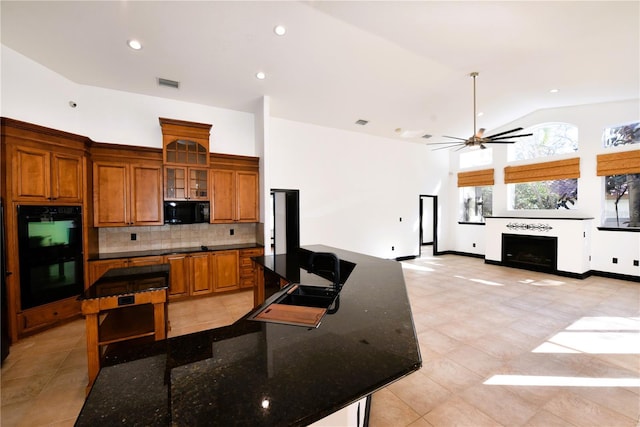 kitchen featuring backsplash, black appliances, a center island, and dark stone counters