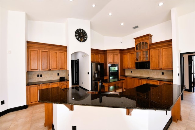 kitchen with fridge with ice dispenser, a kitchen breakfast bar, dark stone counters, and a large island with sink