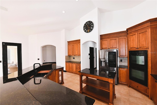 kitchen featuring stainless steel refrigerator with ice dispenser, tasteful backsplash, a center island, high vaulted ceiling, and double oven