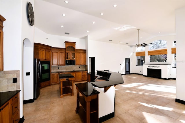 kitchen featuring a breakfast bar, ceiling fan, backsplash, a center island, and black appliances