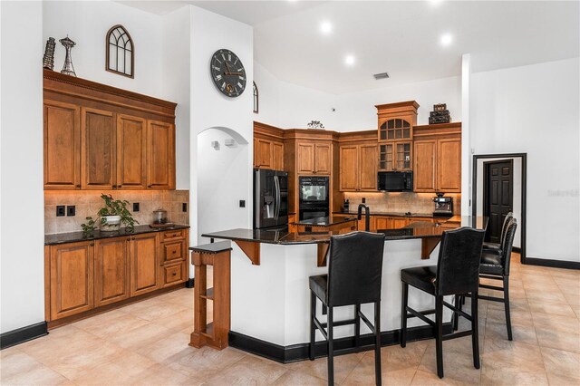 kitchen with a breakfast bar area, black appliances, a center island with sink, dark stone countertops, and a high ceiling