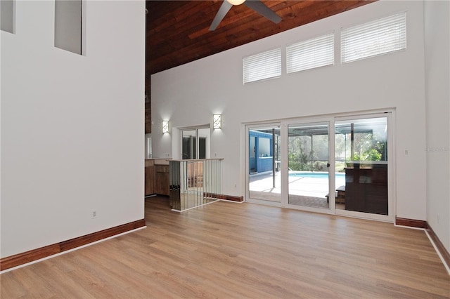 unfurnished living room with ceiling fan, wooden ceiling, a towering ceiling, and light wood-type flooring