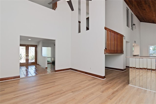 unfurnished living room with a towering ceiling, ceiling fan, light hardwood / wood-style flooring, and french doors