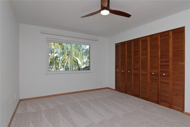 unfurnished bedroom with ceiling fan, light carpet, a closet, and a textured ceiling