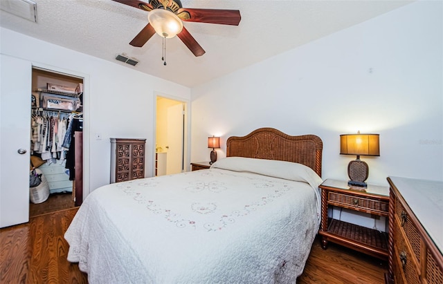 bedroom with dark hardwood / wood-style flooring, a textured ceiling, ceiling fan, a spacious closet, and a closet