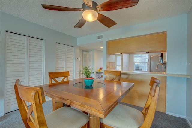 carpeted dining room with a textured ceiling, ceiling fan, and sink