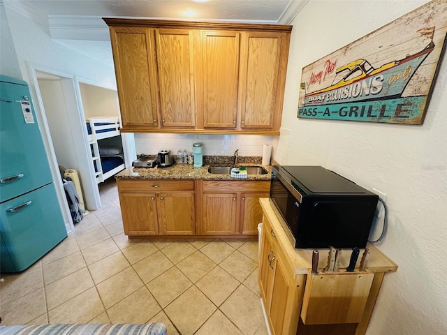 kitchen with light stone counters, backsplash, light tile floors, ornamental molding, and sink