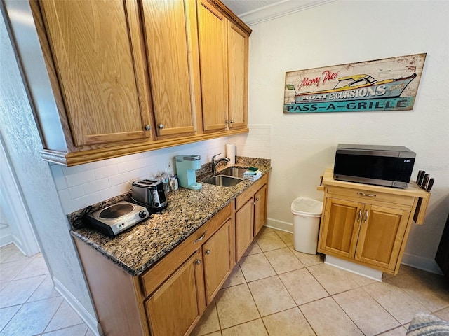 kitchen featuring ornamental molding, dark stone countertops, backsplash, sink, and light tile flooring